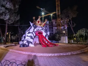 The Golem sculpture with a crown at night, showing a black-and-white patterned figure and three red ramps extending from its mouth.