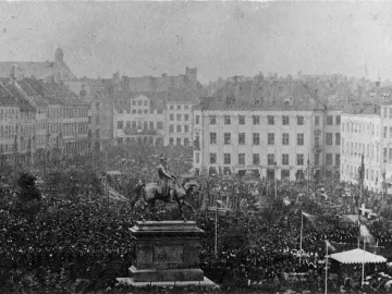 Frederick VII’s equestrian statue stands on a tall pedestal in a crowded city square surrounded by European-style buildings.