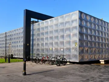 Michael Faraday Memorial with reflective metal panels and a dark rectangular archway, with bicycles parked in front.
