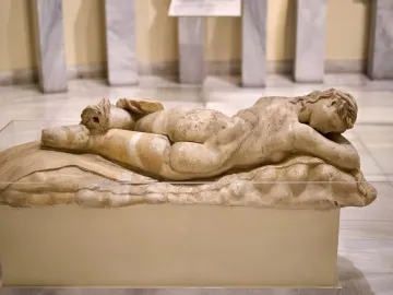 Ancient marble Sleeping Maenad reclining on a pedestal in a museum display.
