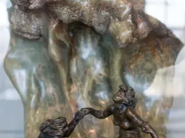 The Wave sculpture with three intertwined bronze figures beside a tall marbled stone form.
