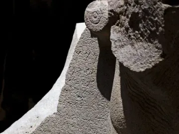 Close-up of the Çineköy inscription carved into light-colored stone, with incised symbols and a sculpted form in strong shadow.