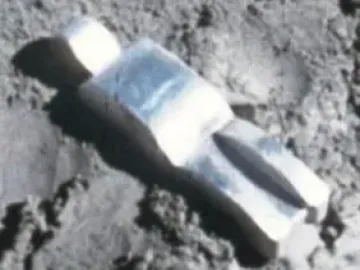Fallen Astronaut figure lying on a textured grey surface, casting a sharp shadow.
