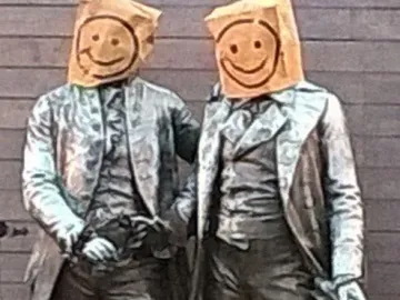 Goethe and Schiller Monument with both figures wearing paper bags over their heads with smiley faces drawn on them.