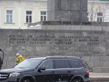 Lower part of the Lenin Monument with Russian text carved into the stone base, with snow falling nearby.