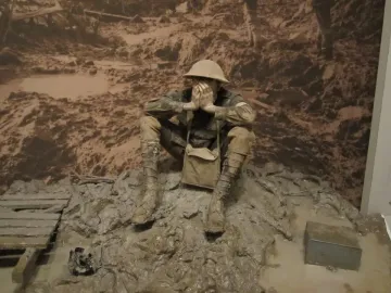 Man in the mud sculpture of a soldier sitting with hands covering his face in muddy terrain.
