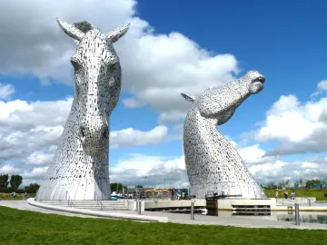 The Kelpies horse head sculptures beside water under a blue sky with clouds.