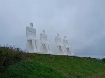 The Man by the Sea sculpture with four white seated figures on a grassy slope under a grey sky.