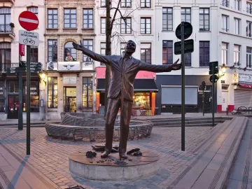 Jacques Brel memorial bronze statue by Tom Frantzen, shown with arms outstretched on a cobblestone square in Brussels.