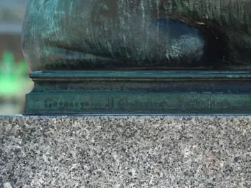 Bronze base of the Sleeping Lion sculpture with a Gladenbeck foundry inscription on a granite pedestal.