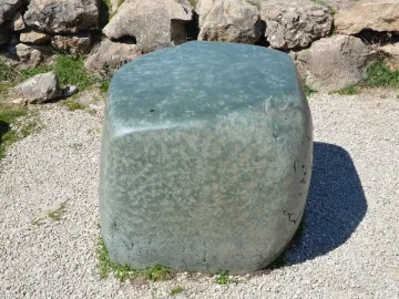 Hattusa Green Stone resting on light gravel beside a rough stone wall and grass