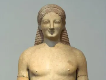 Kouros marble statue of a nude male figure with an archaic smile, long ridged hair, and a missing left forearm.