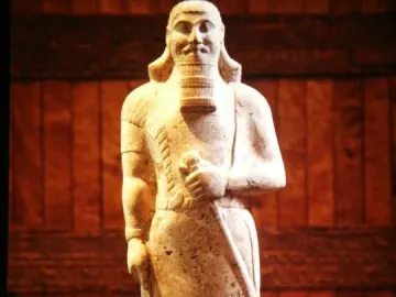 Statue of Ashurnasirpal II with a stylized beard, curly hair, and a long staff held vertically across the body.