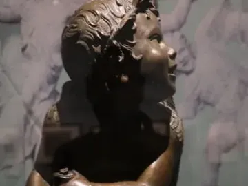 Candelabra Angels, a bronze winged putto seated on an ornate white base and holding a small object while looking upward.