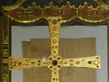 The Cross of the Angels, a jeweled golden cross displayed in a case with two kneeling angel figures beside it.