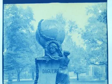 Daguerre Memorial with a bust, globe, and draped female figure on a pedestal in a park