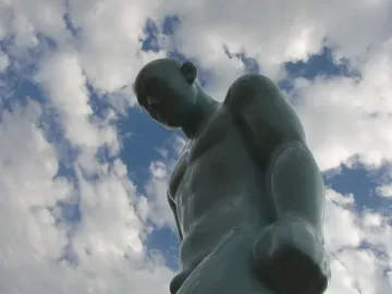 Greetingman statue seen from below against a blue sky with clouds