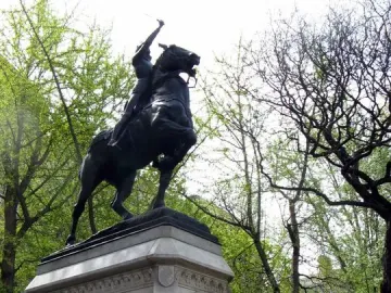Joan of Arc equestrian statue on a tall stone pedestal surrounded by trees.
