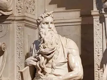 Moses statue seated with tablets, gripping his beard and looking upward.