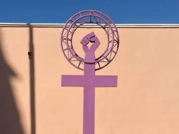 Antimonumenta sculpture in purple, shaped like the Venus symbol with an upright fist on a concrete base.