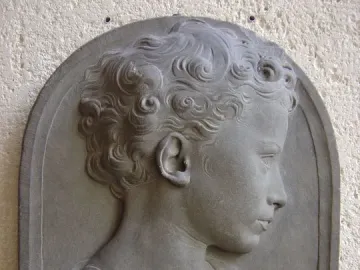 Bust of a Child in profile, showing a curly-haired young figure in draped garments against a dark background.