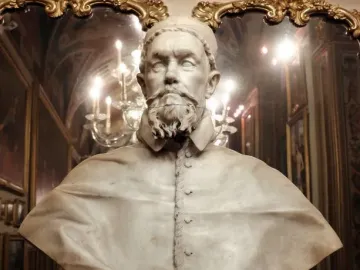White marble bust of Pope Innocent X wearing a clerical cape and cap, displayed on a pedestal in an ornate room.