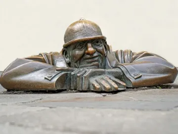 Čumil, a bronze man emerging from a street opening with his hands resting on the rim