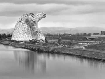 The Kelpies horse head sculptures beside calm water under a cloudy sky.