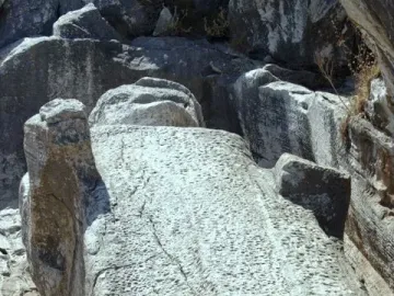 Unfinished Kouros of Apollonas stone statue lying horizontally in a rocky quarry landscape.