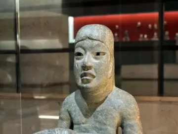 Las Limas Figurine showing a seated grey-green stone figure holding a smaller figure across its lap.