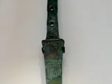 The Spear of Lugal, a tarnished metal artifact with an engraved feline figure and three holes in the handle.