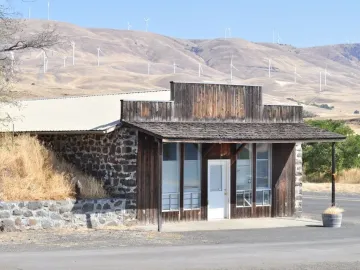 Rustic building at the entrance to Maryhill Stonehenge with wind turbines on the hills behind it.
