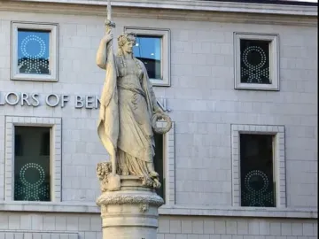 Monumento dell\'Indipendenza, a stone female statue holding a sword and wreath atop a tall pedestal with people seated on the steps below.