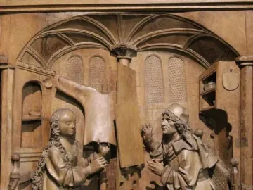 Wooden relief of Saint Luke seated beside the Madonna in an ornate architectural alcove.
