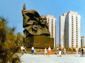 Ernst Thälmann Memorial in a wide public square with apartment buildings behind it and people walking nearby.
