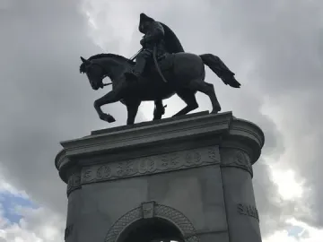 The Sam Houston Statue monument with a bronze rider on horseback above a stone archway, seen from below under a cloudy sky.