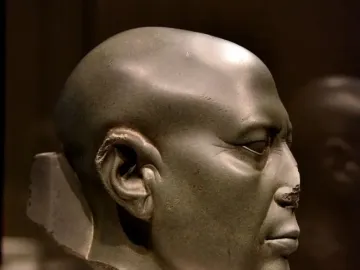 Berlin Green Head shown in right-side profile, a dark greenish-gray stone head with a worn nose and serious expression.