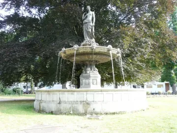 A classical draped female statue stands atop the Diana Fountain as water flows into a stone basin, with trees in the background.