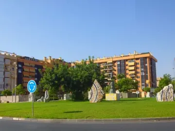Dona Lluna sculpture on a bright yellow base in a grassy roundabout, with a crescent-shaped element at the top.
