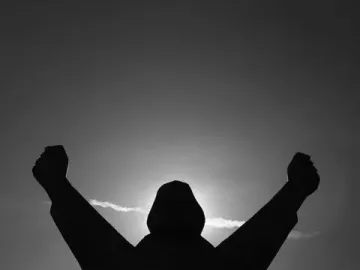 Silhouetted Monument to Stjepan Filipović with arms raised and fists clenched against a bright sky