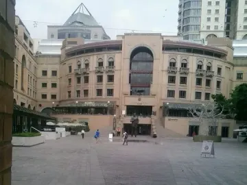 Nelson Mandela statue standing in a paved plaza in front of a large building with an arched window.