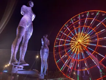 Ali and Nino statues lit in purple beside a brightly lit Ferris wheel at night.