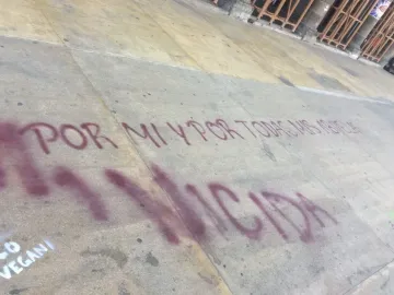Spanish graffiti on a light-colored sidewalk reading \