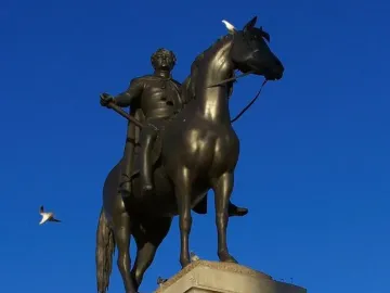 Equestrian Statue of George IV on a stone pedestal with a bronze horse and rider, against a blue sky with birds nearby.