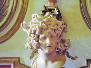 Marble bust of Medusa with coiled snakes for hair and a pained expression, displayed on a pedestal.