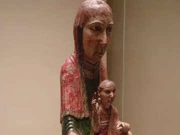 Virgin from Ger, an aged carved wooden figure of a woman holding a smaller figure on her lap, with faded red and green paint and a long veil.