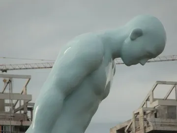 Greetingman sculpture with a pale blue figure bowing deeply under a cloudy sky.