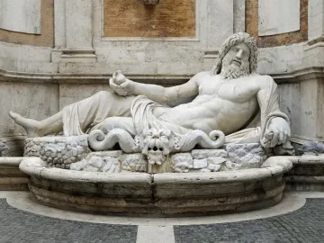 Marforio marble fountain statue reclining on a rocky base with a grotesque face spouting water below.