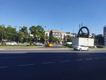 Hittite Sun Disk Monument on a white base in an urban street with cars and buildings in the background.
