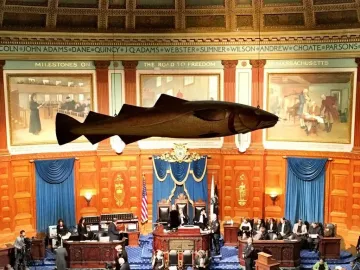 The Sacred Cod hangs above seated lawmakers in a wood-paneled legislative chamber.